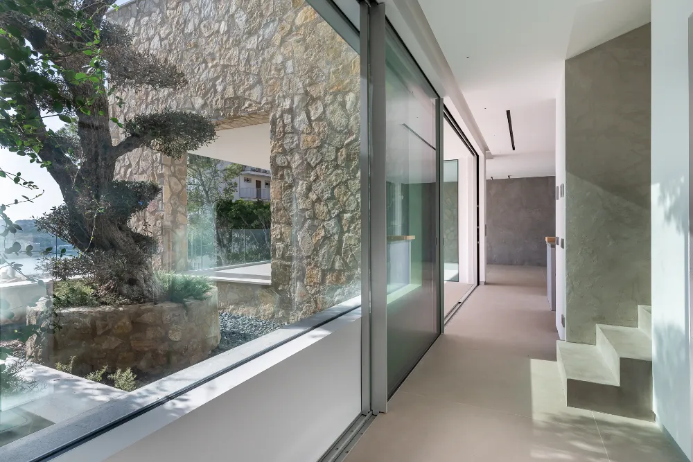 Interior hallway with natural stone wall, glass doors and contemporary staircase