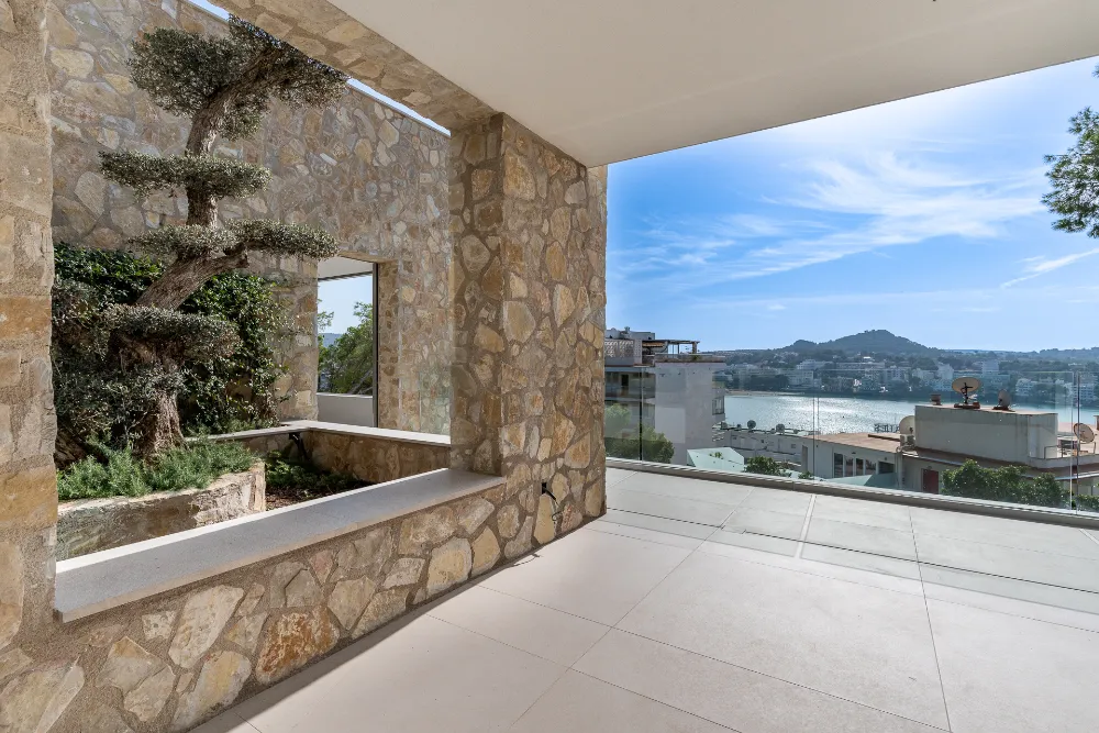 Covered outdoor terrace with stone columns, olive tree and bay views