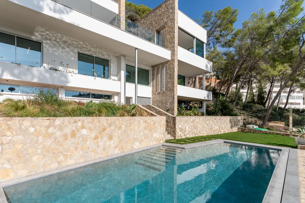 Swimming pool in front of the modern villa facade and stone garden wall